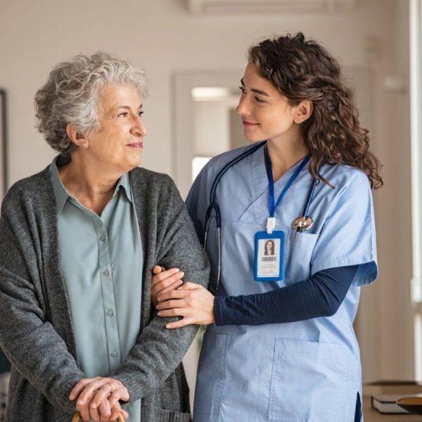 Young caregiver helping senior woman walking. Nurse assisting her old woman patient at nursing home. Senior woman with walking stick being helped by nurse at home.